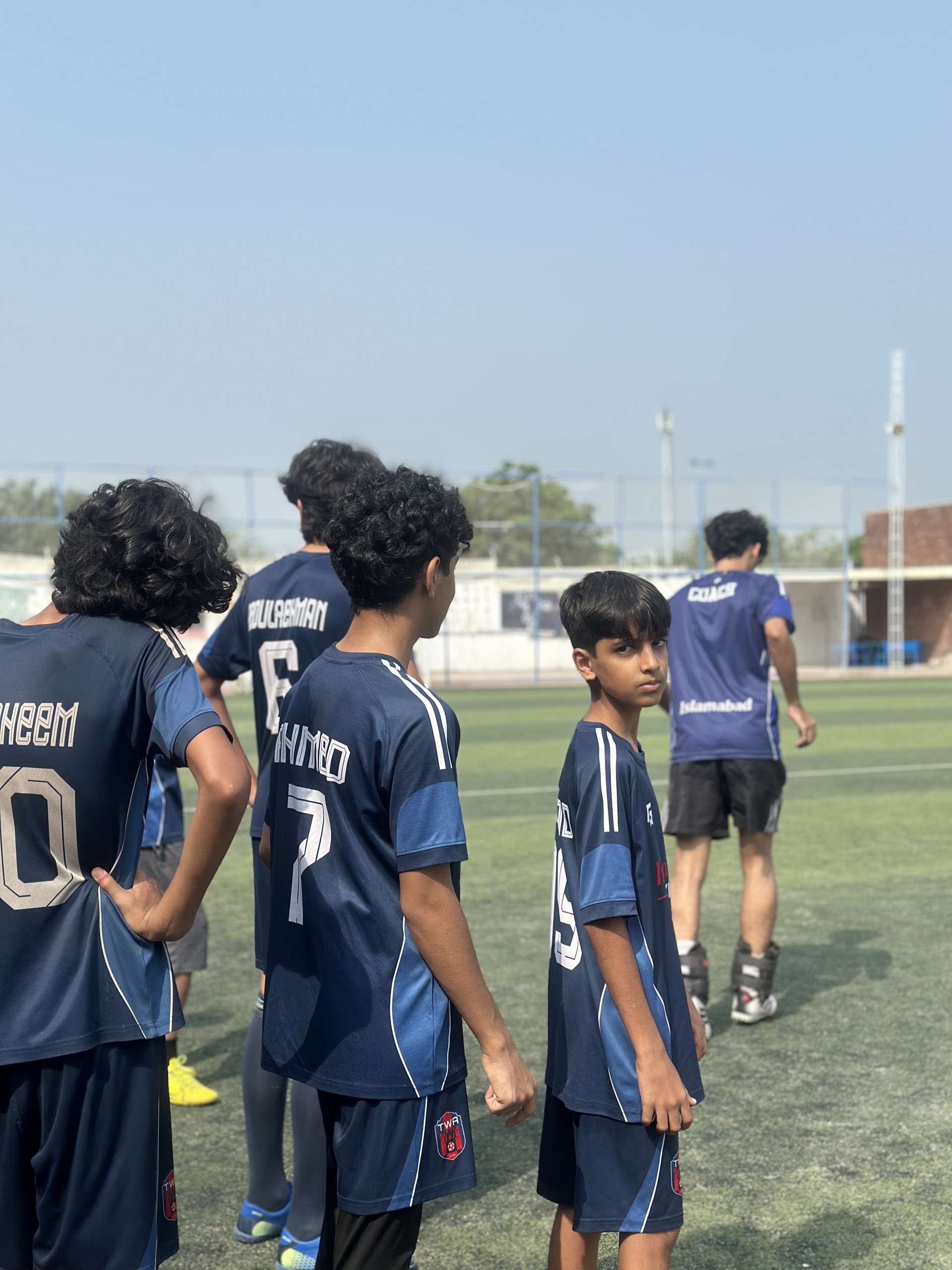 The squad in a huddle, backs to camera, numbers showing on the navy shirts